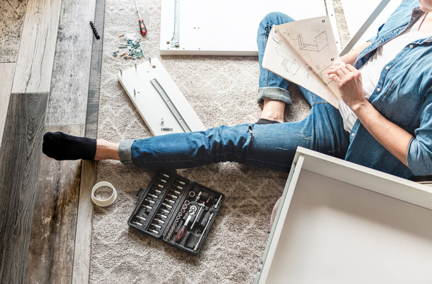 Man sitting on floor and reading manual to assemble diy furniture at home - Foto, immagini