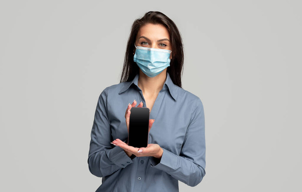 Young woman in medical mask showing smartphone - Foto, afbeelding
