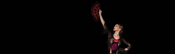 panoramic crop of beautiful dancer looking at fan while dancing flamenco isolated on black  - Фото, изображение
