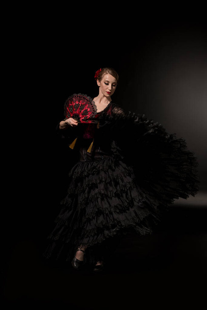 joven bailarina de flamenco sosteniendo abanico y bailando sobre negro
  - Foto, Imagen