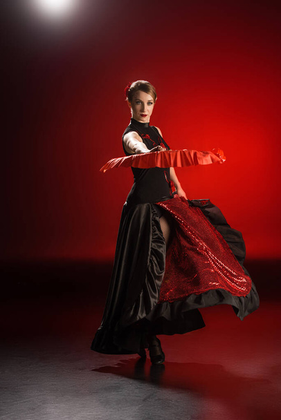 elegant woman in dress holding fan while dancing flamenco on red  - Photo, Image