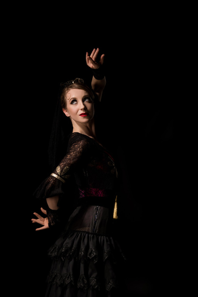 κομψός χορευτής φλαμένκο κοιτάζει αλλού και χορεύει απομονωμένος στα μαύρα  - Φωτογραφία, εικόνα