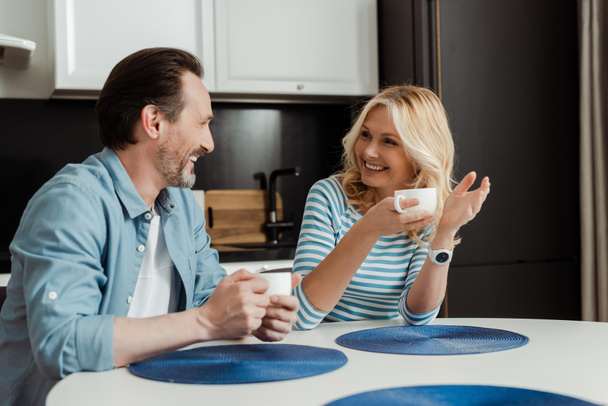 Mature couple smiling at each other while drinking coffee at home  - Photo, image