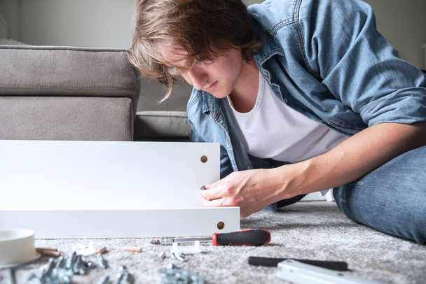 Concentrated young man assembling new furniture for home - Foto, Bild