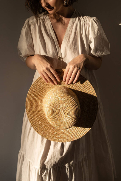 Young pretty woman in white dress / sundress holding straw hat. Minimal fashion design concept. - Фото, зображення