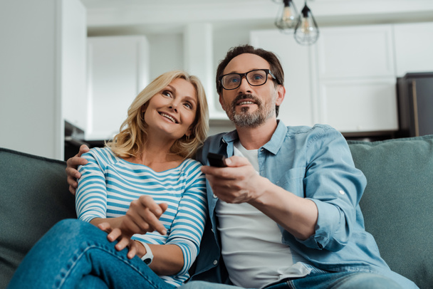 Выборочный фокус улыбающейся зрелой пары, смотрящей телевизор на диване
  - Фото, изображение