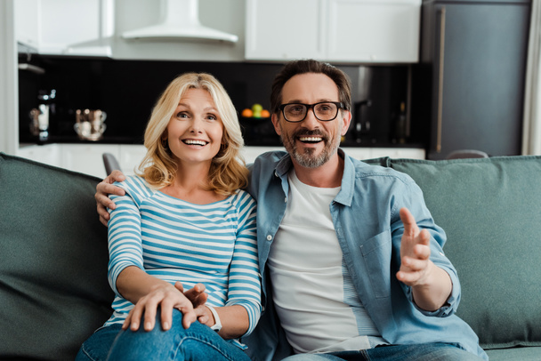 Selective focus of handsome man embracing beautiful smiling wife on couch  - Fotoğraf, Görsel