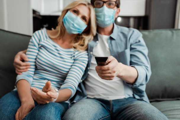 Selective focus of mature couple in medical masks watching tv at home  - Foto, Imagem