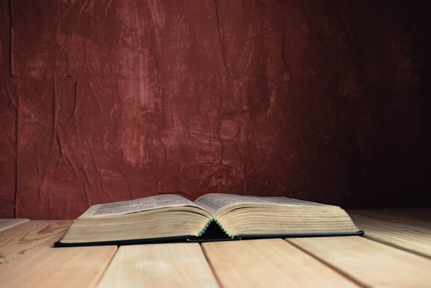 Open Holy Bible on a old wooden table. Beautiful red wall background.	 - 写真・画像