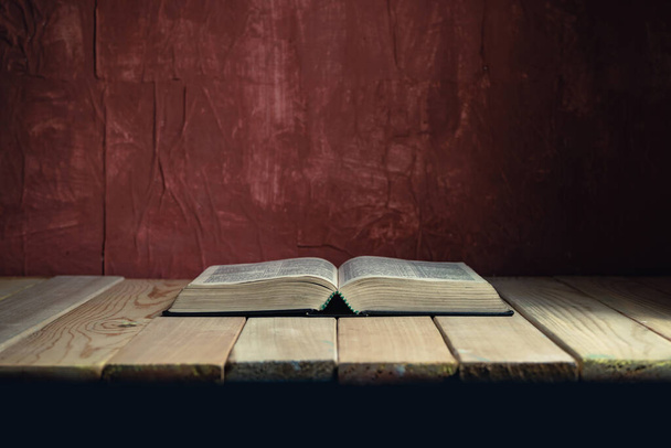 Open Holy Bible on a old wooden table. Beautiful red wall background.	 - Fotografie, Obrázek