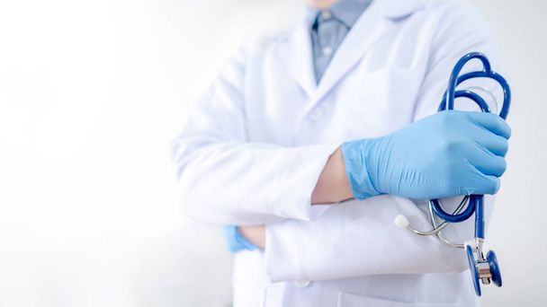 Sanità e concetto medico. Medico asiatico maschio con stetoscopio in mano. Medico con camice bianco e guanti blu che lavora in clinica durante la pandemia di Coronavirus (COVID-19)
. - Foto, immagini