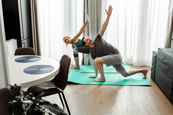 Выборочный фокус улыбающейся зрелой пары, работающей на фитнес-ковриках в гостиной
 - Фото, изображение