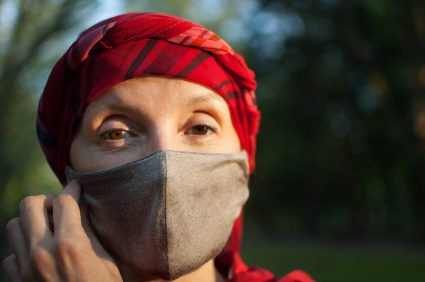 Mature woman wearing handmade textile face mask as accessory and protective element during sunny spring day in the park because of coronavirus pandemic - Фото, зображення