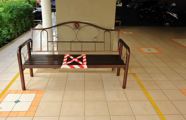 Detailní červené pruhy barikádní páska označená křížovým symbolem na lavičce ukázat zakázané místo pro sezení, fyzické distancování, nový normální koncept v důsledku pandemie koronaviru  - Fotografie, Obrázek