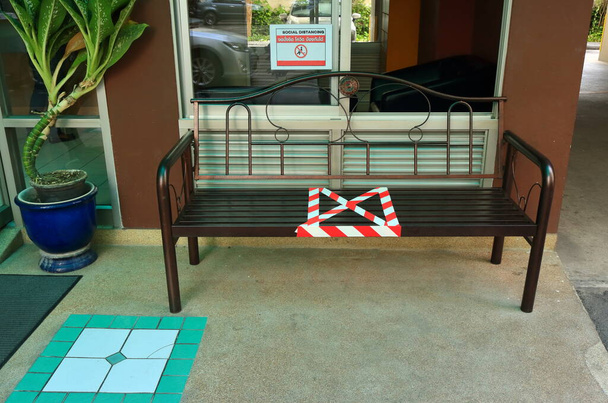 Pusta ławka przed budynkiem oznaczonym czerwonym białym paskiem taśmą barykadową, aby pokazać zakazane miejsce do siedzenia, dystans społeczny, nowa normalna koncepcja z powodu pandemii koronawirusowej  - Zdjęcie, obraz