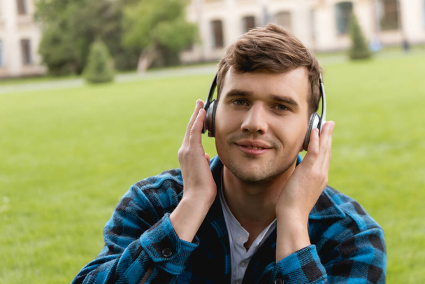 Mutlu öğrenci kablosuz kulaklıklara dokunuyor ve müzik dinliyor  - Fotoğraf, Görsel