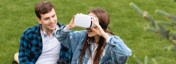 panoramic shot of cheerful student looking at happy girl in virtual reality headset  - Foto, Imagem