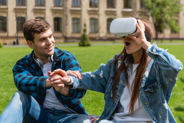 wesoły student trzymając się za ręce z zaskoczoną dziewczyną w wirtualnej rzeczywistości zestaw słuchawkowy  - Zdjęcie, obraz