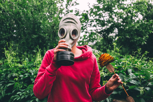 Chica tratar de sacar goma máscara de gas vintage para oler flor de madera artificial, la vida en pandemia, coronavirus, epidemia, guerra nuclear, concepto del fin del mundo, colores brillantes al aire libre
  - Foto, imagen