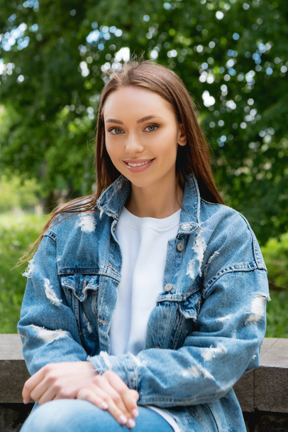 selective focus of cheerful girl in denim jacket looking at camera - Photo, Image