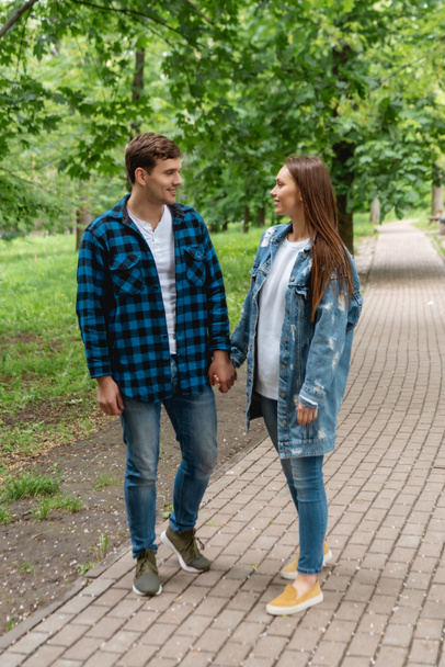 cheerful couple of students holding hands and looking at each other in park  - Foto, Imagem