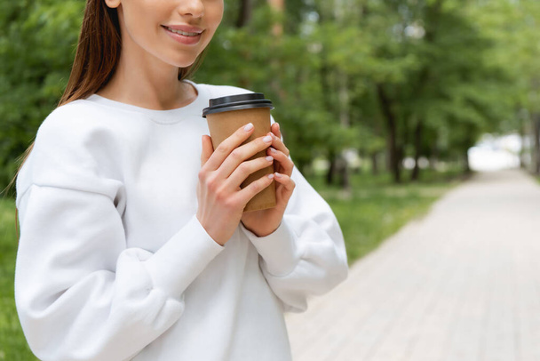 vista recortada de chica feliz sosteniendo café para ir en taza de papel
  - Foto, Imagen