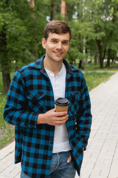 pohledný student stojící s rukou v kapse a drží papírový šálek  - Fotografie, Obrázek