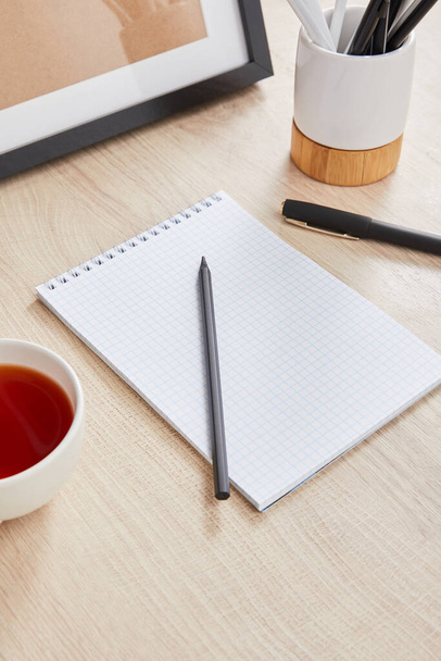 xícara de chá e caderno em branco com lápis e caneta na superfície de madeira
 - Foto, Imagem