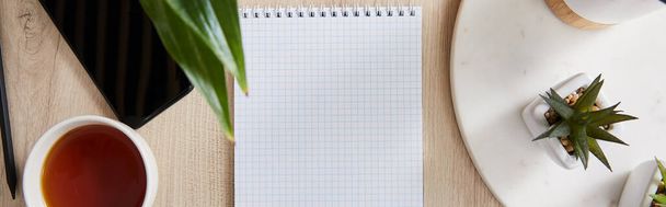 Draufsicht auf grüne Pflanzen, Tasse Tee und leeres Notizbuch mit Bleistift und Smartphone auf Holzoberfläche, Panoramaaufnahme - Foto, Bild