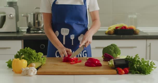 Nainen viipaloi ison pippurin keittiön pöydälle. Salaatin valmistus. 4K - Materiaali, video
