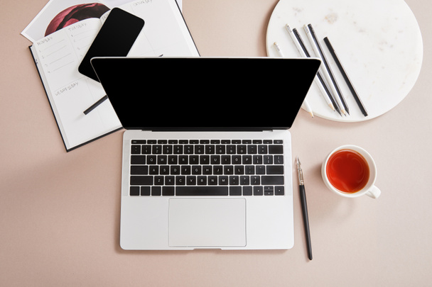 top view csésze tea, laptop, tervező, kártya, okostelefon közelében kör ceruzák bézs felületen - Fotó, kép