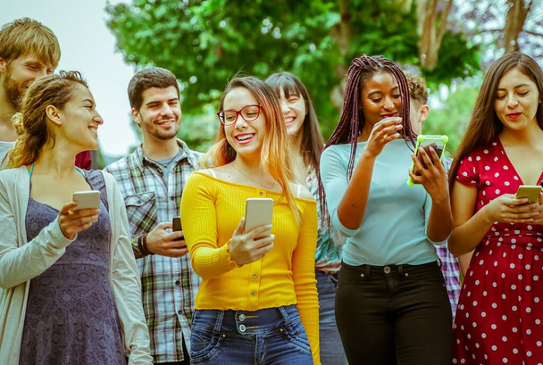 Amigos felices usando teléfonos inteligentes: estudiantes jóvenes que se divierten con la tecnología. Amistad y concepto universitario - Imagen
 - Foto, imagen
