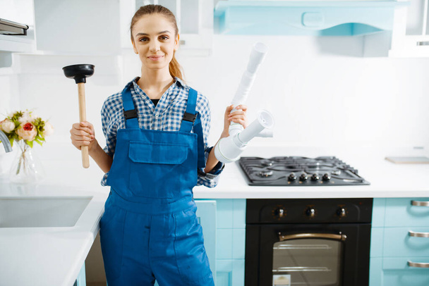 Nette Installateurin in Uniform hält Kolben und Rohr, verstopft die Küche. Handarbeiterin repariert Waschbecken, Sanitärservice zu Hause - Foto, Bild