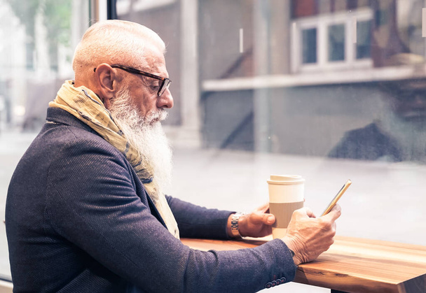 Trendiger Senior mit Smartphone-App in Bar-Cafeteria drinnen - Älterer Mann trinkt Kaffee - Technik und lebensfrohes Senioren-Lifestylekonzept - Image - Foto, Bild