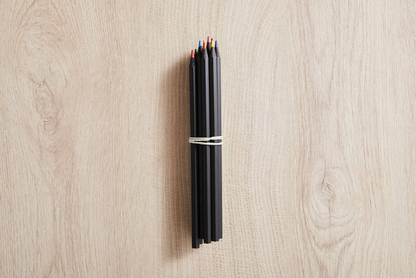 top view of black colored pencils on wooden beige surface - Foto, imagen