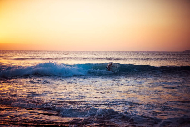 Sylwetka surfera jeżdżącego na fali w pustym miejscu do surfowania. Młody surfer jeździ na fali podczas zachodu słońca. Zdjęcie. - Zdjęcie, obraz