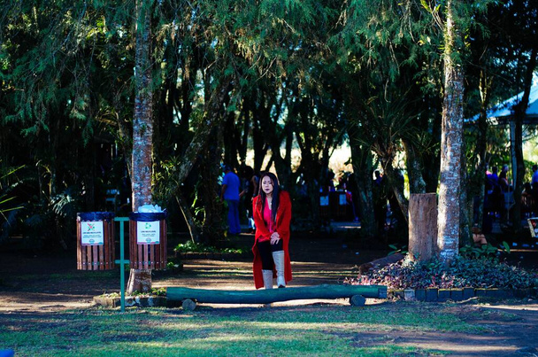 Eine reife Frau in ihren Fünfzigern in stylischer Kleidung, roten Overalls und beigen Lederstiefeln posiert vor einer Freifläche im Park. - Foto, Bild