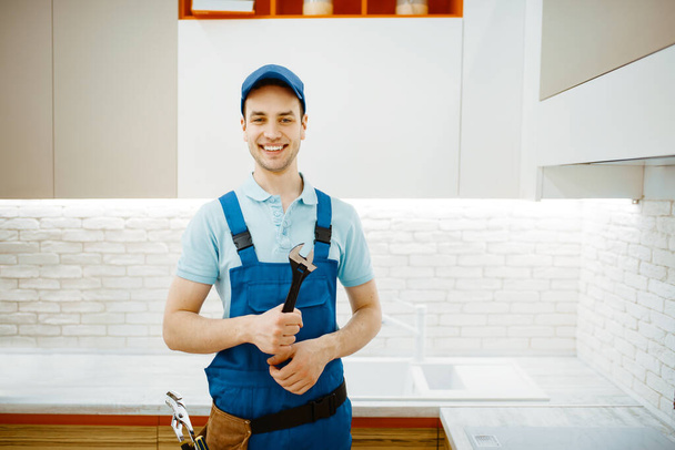 Mannelijke loodgieter in uniform bevestigingskraan in de keuken. Handyman met gereedschapstas reparatie spoelbak, sanitaire apparatuur service thuis - Foto, afbeelding