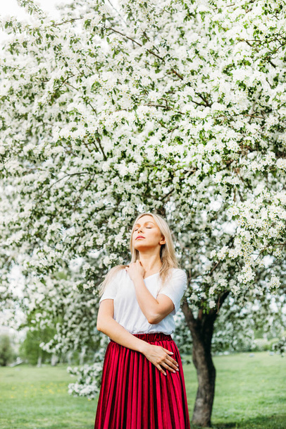Beautiful girl with light hair, glasses, near flowering trees, Apple tree, spring, branches, flower, fashion, style, European, red - 写真・画像