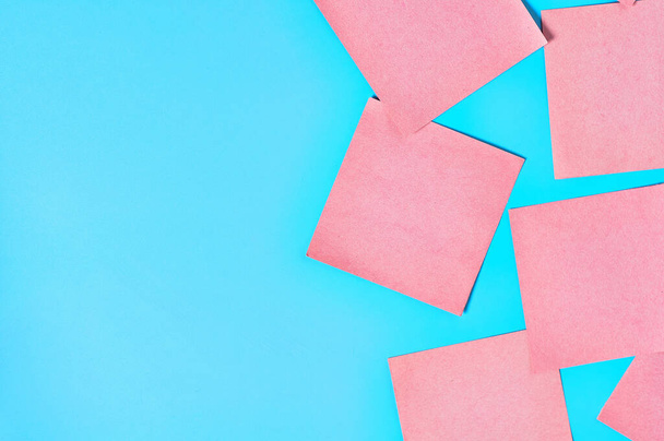 Scattered many pink square blank paper stickers on blue background. Copy space. Top view - 写真・画像