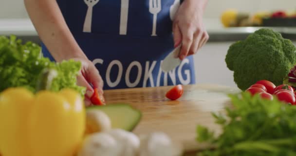 Nahaufnahme. Eine Frau schneidet Kirschtomaten auf einem Küchentisch. Es gibt viel Gemüse. 4K - Filmmaterial, Video