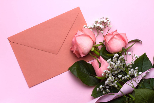Pembe arka planda bir zarf ve güllerin kompozisyonu, yakın plan. Düğün tasarımı, selamlar, davetiyeler, duvar kağıtları. - Fotoğraf, Görsel