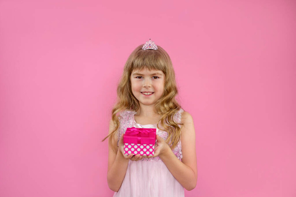 Vaaleanpunainen tyttö, jolla on lahja. Tyttöjen syntymä Pikkutyttö, jolla on lahja kädessään. Lapsella on lahjapakkaus käsissään. Syntymäpäivälahja. - Valokuva, kuva