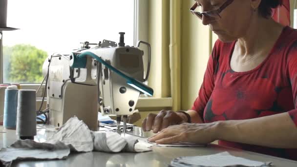 Vrouw gebruikt de naaimachine om het gezichtsmasker te naaien tijdens de coronavirus pandemie. Huishoudelijk maatwerk als gevolg van het tekort aan medisch materiaal. - Video