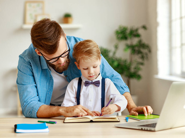 Смарт-маленький хлопчик, який пише в книзі і пояснює навчальне завдання, при цьому зосереджений батько сидить поруч під час онлайн-уроку з ноутбуком вдома
 - Фото, зображення
