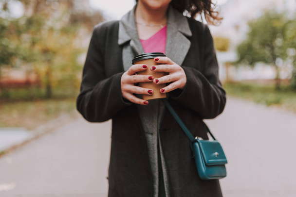 Ausgeschnittenes Foto im Freien. Hände einer Frau mit roter Maniküre halten eine Papptasse Kaffee - Foto, Bild