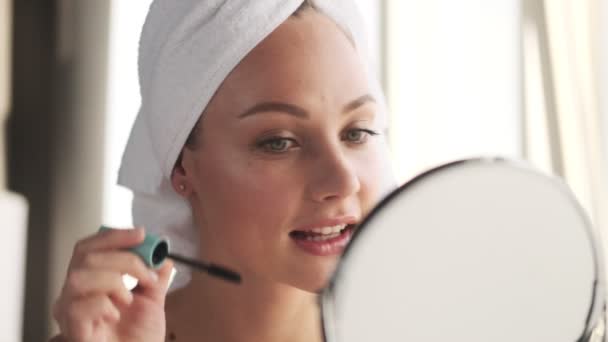 Young pleased happy woman indoors at home apply makeup looking at mirror - Video, Çekim