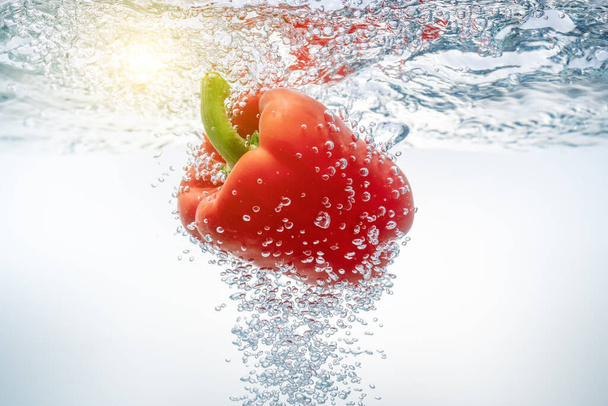 Fallende rote Paprika in ökologisch sauberem Wasser, durch das die Sonne durchbricht. Nahaufnahme. - Foto, Bild