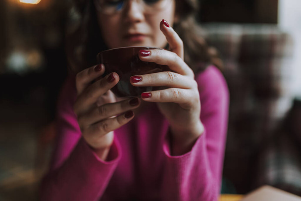 Close up of beautiful lady wearing glasses and sitting in cafe with hot drink in he hands - Foto, afbeelding