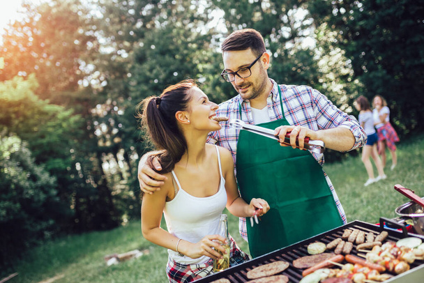 Happy friends grilling meat and enjoying barbecue party outdoors - Фото, зображення